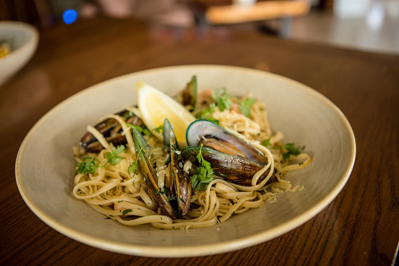 A plate of mussels served on spaghetti pasta with a lemon wedge as garnish