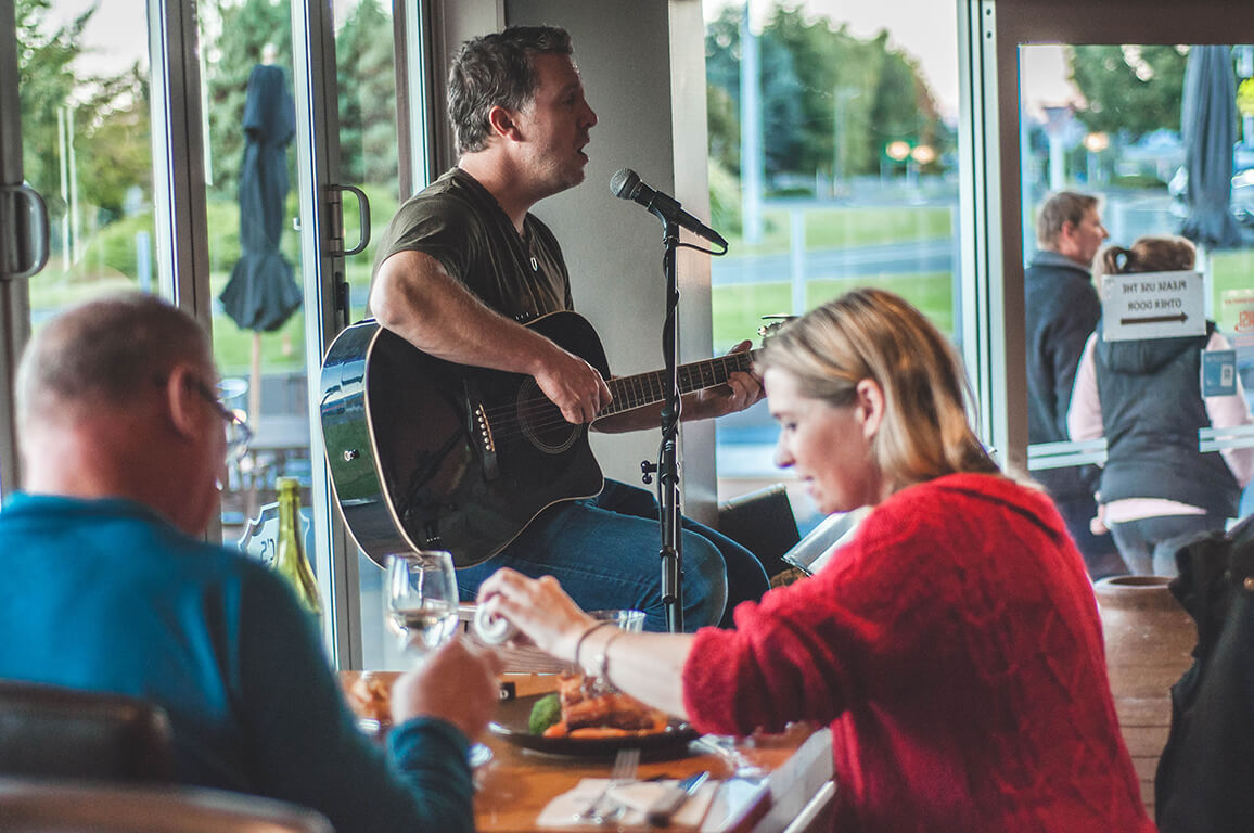 A couple enjoying their meal while listening to a solo musician playing live guitar music at the Fat Duck Te Anau.
