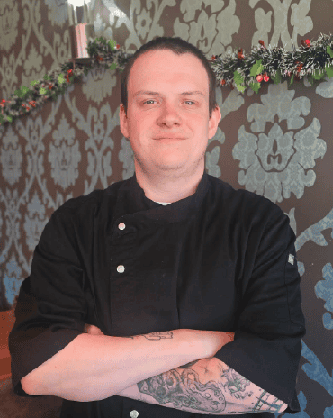 Chef Cody standing inside The Fat Duck Te Anau restaurant wearing a black chef uniform with arms crossed.