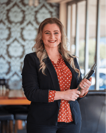 Haylee from The Fat Duck Te Anau standing in the restaurant dining area holding a tablet.
