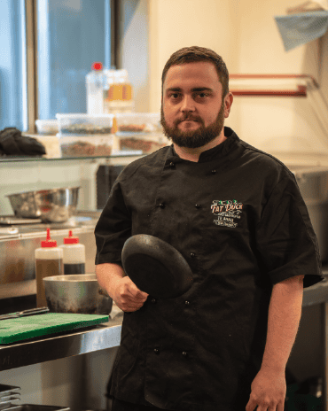 Chef Josh in The Fat Duck Te Anau kitchen holding a pan, preparing dishes for service.